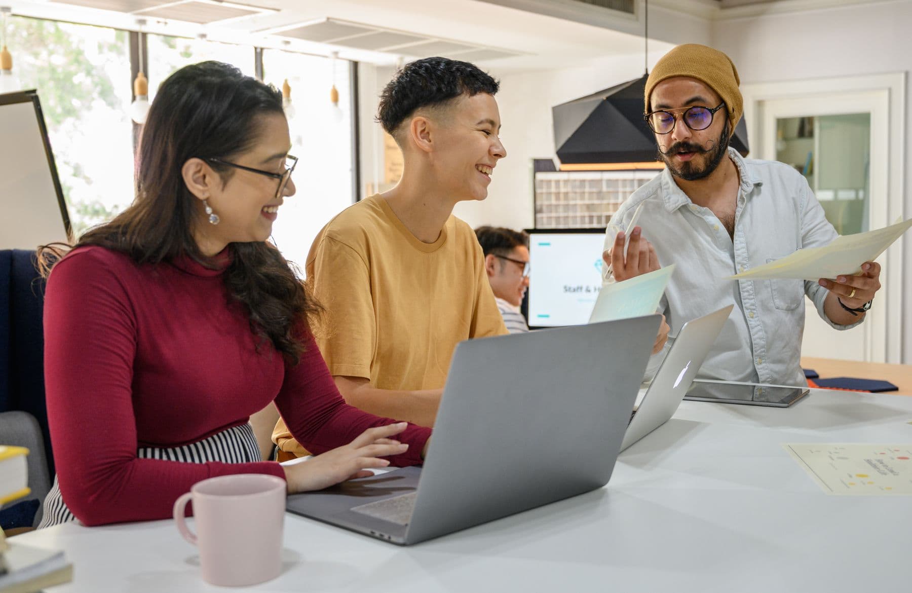 Three people exchanging ideas around laptops and notes.