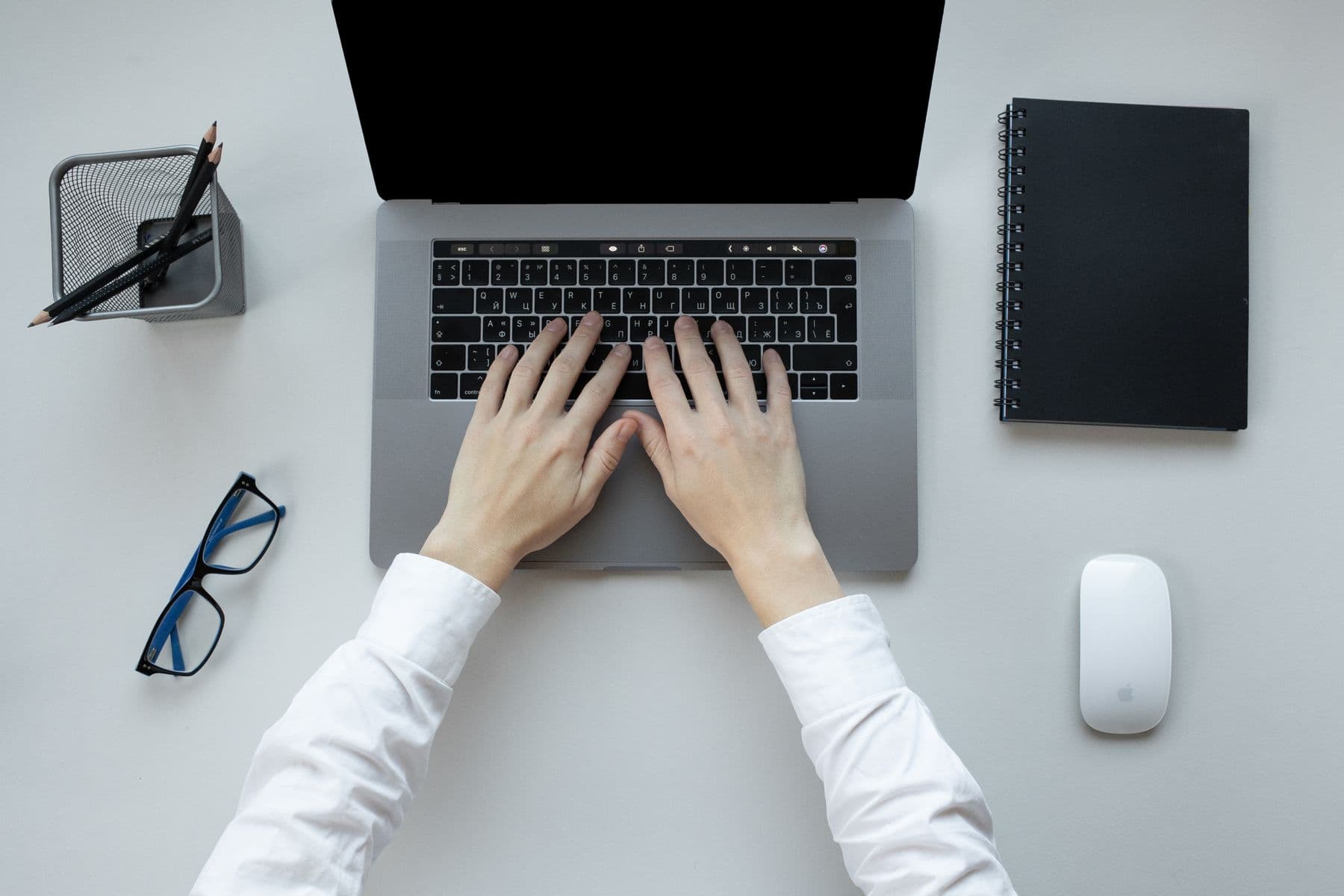 Hands typing on a laptop beside a notebook and glasses.
